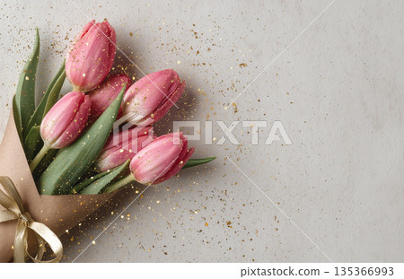 Pink tulips arranged in a bouquet with golden sparkles on a light background during spring 135366993