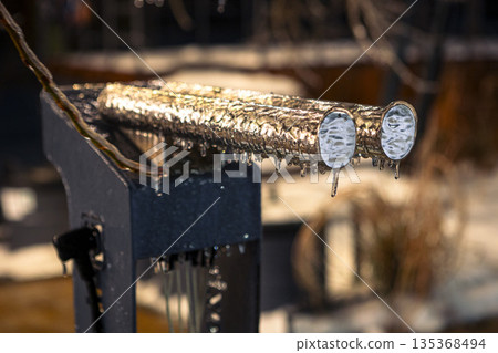 A metal mechanism in the form of two pipes covered with ice in the evening A metal mechanism in the form of two pipes covered with ice in the evening 135368494