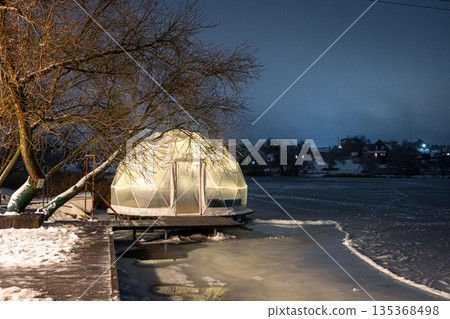 Modern illuminated dome structure on a frosty river bank. Winter luxury relaxation. 135368498