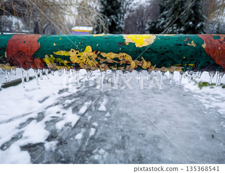 A close-up of a multi-colored metal barrier covered with frost, ice and hanging icicles A close-up of a multi-colored metal barrier covered with frost, ice and hanging icicles 135368541