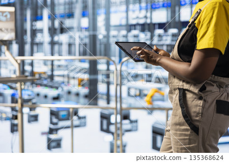 Close up of technician inspecting industrial equipment and machinery on factory floor using tablet app. Worker checking maintenance requirements for automated production units with device 135368624