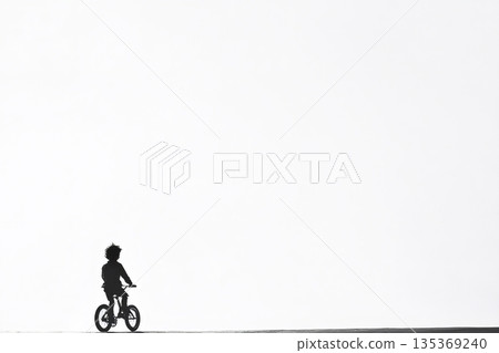 Black and white silhouette of child riding bicycle against vast white background, conveying concepts of freedom, childhood, and simplicity 135369240
