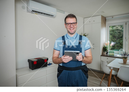 HVAC technician holding digital tablet checking apartment air conditioner HVAC technician holding digital tablet checking apartment air conditioner 135369264