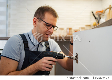 Handyman installing kitchen cabinet door using electric drill Handyman installing kitchen cabinet door using electric drill 135369373