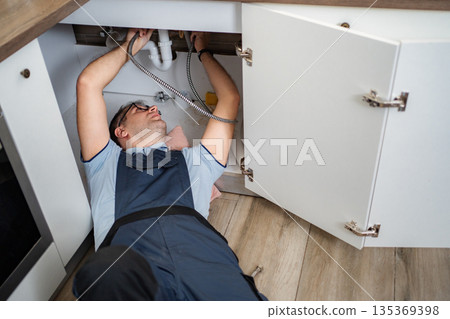 Plumber fixing kitchen sink drain under cabinet 135369398