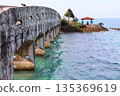 A resting place with a stone bridge over the sea and a red roof 135369619
