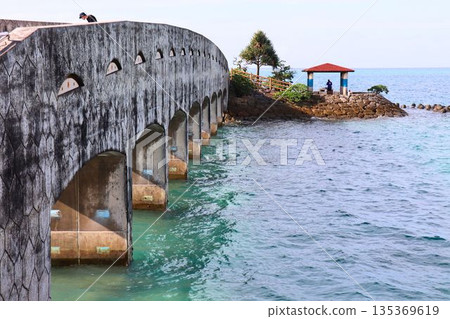 一處休憩之所，有一座橫跨大海的石橋和一座紅色的屋頂。 135369619