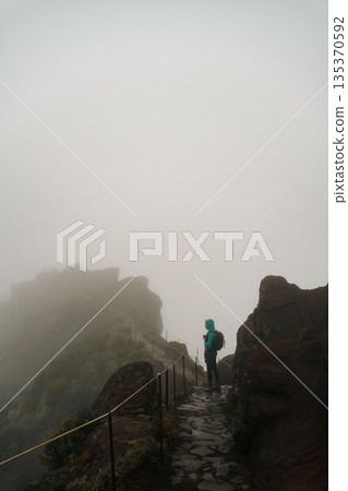 Traveler navigates slippery rocks amid dense fog and muted scenery 135370592
