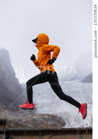 Fitness woman trail runner running in grassland with snow capped mountains in the background Fitness woman trail runner running in grassland with snow capped mountains in the background 135370634