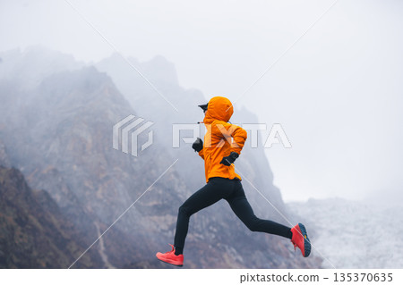 Fitness woman trail runner running in grassland with snow capped mountains in the background Fitness woman trail runner running in grassland with snow capped mountains in the background 135370635
