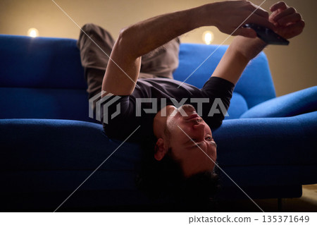 Chilled man on sofa, Casual individual reclining on sofa engrossed with mobile device, Unwinding man sits comfortably on sofa focused on his smartphone amid cozy modern decor Chilled man on sofa, Casual individual reclining on sofa engrossed with mobile device, Unwinding man sits comfortably on sofa focused on his smartphone amid cozy modern decor 135371649
