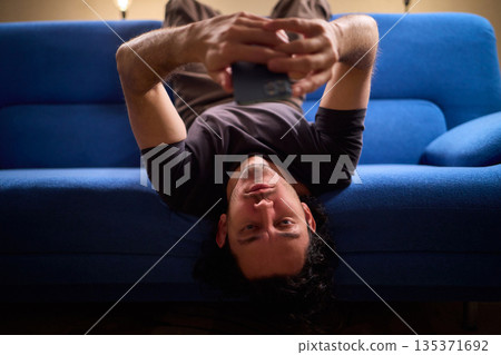 Chilled man on sofa, Casual individual reclining on sofa engrossed with mobile device, Unwinding man sits comfortably on sofa focused on his smartphone amid cozy modern decor Chilled man on sofa, Casual individual reclining on sofa engrossed with mobile device, Unwinding man sits comfortably on sofa focused on his smartphone amid cozy modern decor 135371692