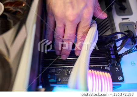 Detailed view of mounting RAM modules into motherboard slots carefully, Closeup of hands placing RAM securely into motherboard black slots with subtle lighting effects 135372193