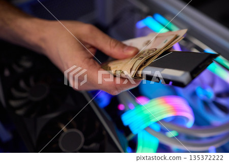 Hidden cash stored in computer memory modules, Covert operation involving cash hideaway inside memory hardware amid colorful RGB illumination and mining equipment 135372222