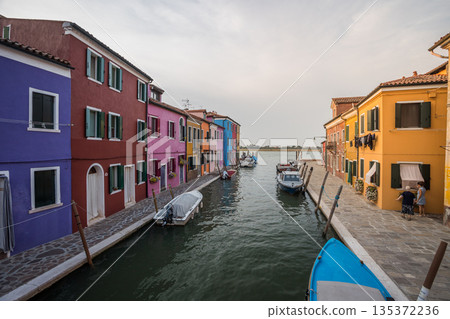 Colorful canal street on Burano island near Venice with vibrant traditional houses, small boats, calm waterway, and authentic Italian lagoon atmosphere under soft evening light 135372236
