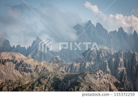 Dramatic alpine landscape of the Dolomites near Tre Cime di Lavaredo with jagged limestone peaks emerging through soft clouds in a serene high altitude mountain wilderness 135372250