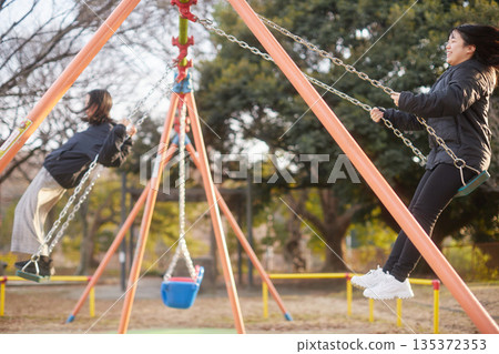 冬夜裡,兩個可愛的國中女生在公園的鞦韆上玩耍 冬夜裡,兩個可愛的國中女生在公園的鞦韆上玩耍 135372353