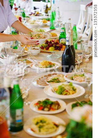 Long table set for meal with various dishes and drinks 135372358