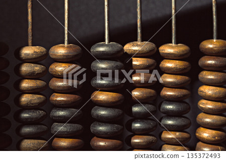 Wooden beads are strung on metal rods in a dark setting under a light Wooden beads are strung on metal rods in a dark setting under a light 135372493