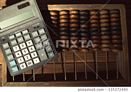 Calculator and abacus sit on a wooden surface in a study space during afternoon light Calculator and abacus sit on a wooden surface in a study space during afternoon light 135372495
