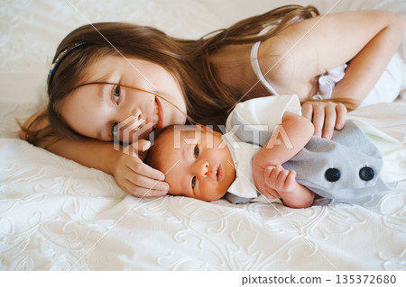 Sister and baby brother share a moment on a bed 135372680