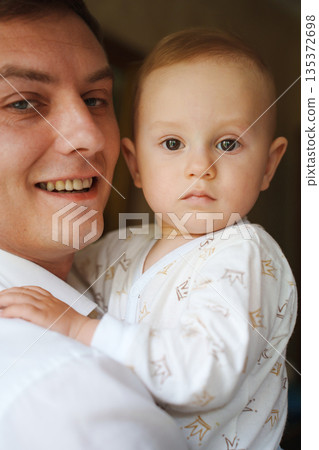 Father holding baby with a gentle smile at home 135372698