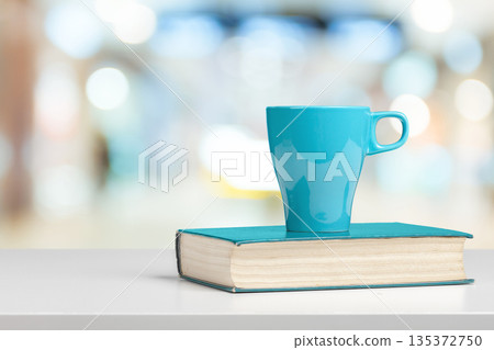 Cup of beverage placed on a book in a bright indoor space with blurred background 135372750