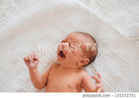 Newborn baby yawning on a soft blanket in a room Newborn baby yawning on a soft blanket in a room 135372751