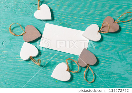 Decorative hearts surround a blank card on a wooden table 135372752
