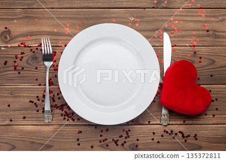 Set table with white plate, silver fork, knife, and red heart shape on wood background 135372811