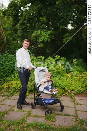 Father pushing stroller with happy child in park setting Father pushing stroller with happy child in park setting 135372812