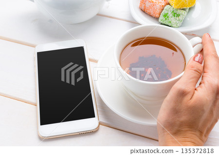 Enjoying a warm drink while using a smartphone in a cafe setting during the day Enjoying a warm drink while using a smartphone in a cafe setting during the day 135372818