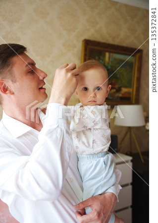 Father gently combs baby hair in cozy room 135372841