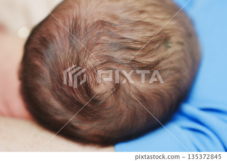 Close view of baby's head on caregiver's arm 135372845
