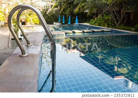 Swimming pool with steps and reflections in a garden area during daylight hours Swimming pool with steps and reflections in a garden area during daylight hours 135372911