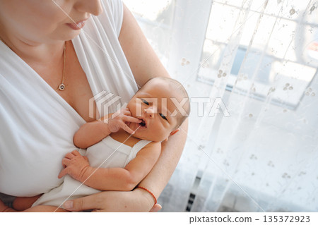 Newborn baby in mother's arms at home in sunlight 135372923