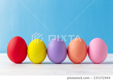 Colorful eggs arranged in a line on a light surface against a blue background Colorful eggs arranged in a line on a light surface against a blue background 135372944
