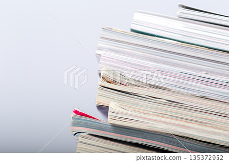 Piles of assorted papers placed on a flat surface in a bright area at a workspace 135372952