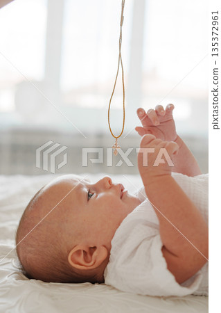 Baby reaching for a necklace while lying on the bed 135372961