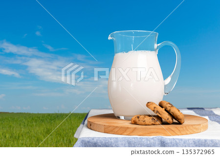 Milk and cookies sit on a table in a field under a blue sky during the day 135372965