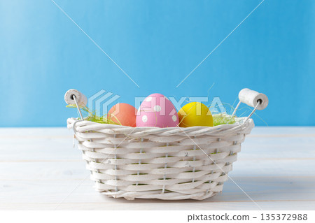 Colorful eggs in a white basket on a blue background during spring season Colorful eggs in a white basket on a blue background during spring season 135372988