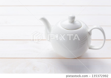 White teapot placed on a wooden surface in a simple setting during daylight hours 135372992