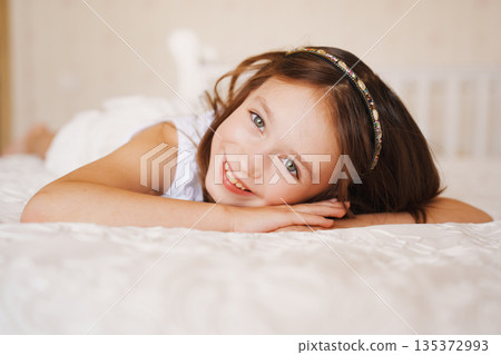 Young girl smiles while lying on bed in bright room 135372993