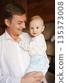 Smiling man holds baby in cozy indoor setting 135373008
