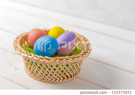 Colorful eggs in a basket on a white wooden table for a spring event 135373051