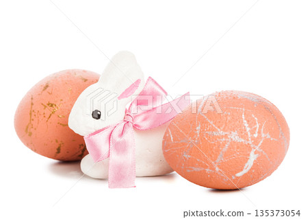 White bunny with pink bow next to two decorated eggs on white background 135373054