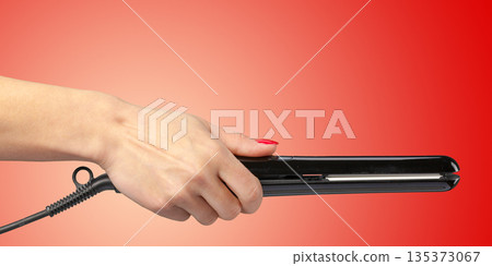 Person holds a hair straightener with a red background during a beauty routine Person holds a hair straightener with a red background during a beauty routine 135373067