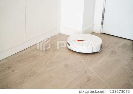 Autonomous robot vacuum cleaner cleaning hardwood floor under sofa in modern apartment with smart home technology 135373073