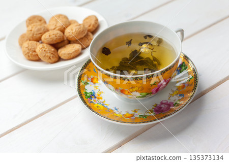 Warm tea and cookies on a white table with a floral cup and saucer in a cozy setting 135373134