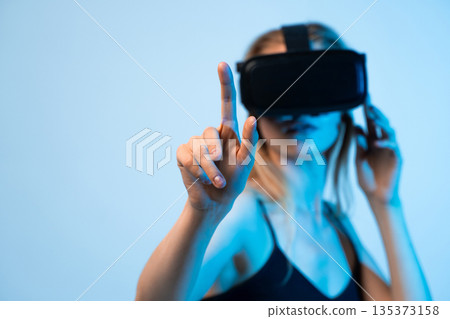 Young woman experiencing virtual reality and interacting with digital interface, common VR technology concept Young woman experiencing virtual reality and interacting with digital interface, common VR technology concept 135373158